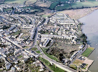 Taken from above the Waterside south of the bridges and looking north, this photo shows an area where there have been many changes in the last three or four decades. Towards the left are the roundabout at the end of the Tamar Bridge, the old North Road School, the old Working Men's Club, and the open area between the houses on North Road and Belle Vue Road, all now replaced by the deep cutting leading into the A38 tunnel. In the right foreground we see a large open area of allotments, now covered by a housing development. In the distance to the right is the large triangle of bare and unused reclaimed land which would later become Saltmill Park, and the open fields in the centre distance are now pierced by the A38 bypass.